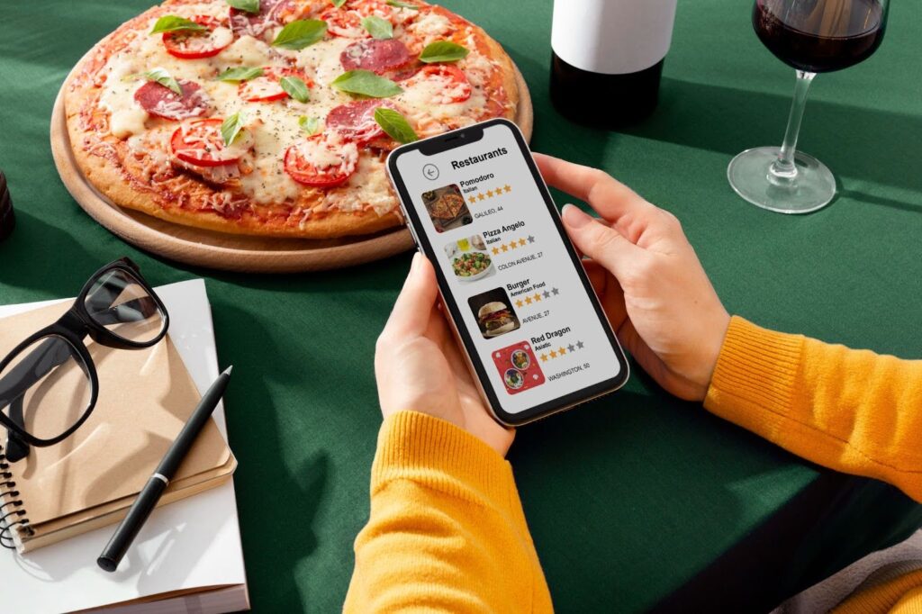 Person browsing restaurant options and online ordering on a smartphone next to a pizza on a dining table.